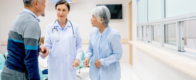 Doctor speaking with an elderly couple in a bright hospital reception area, highlighting compassionate patient care, staff communication, and a welcoming healthcare environment.