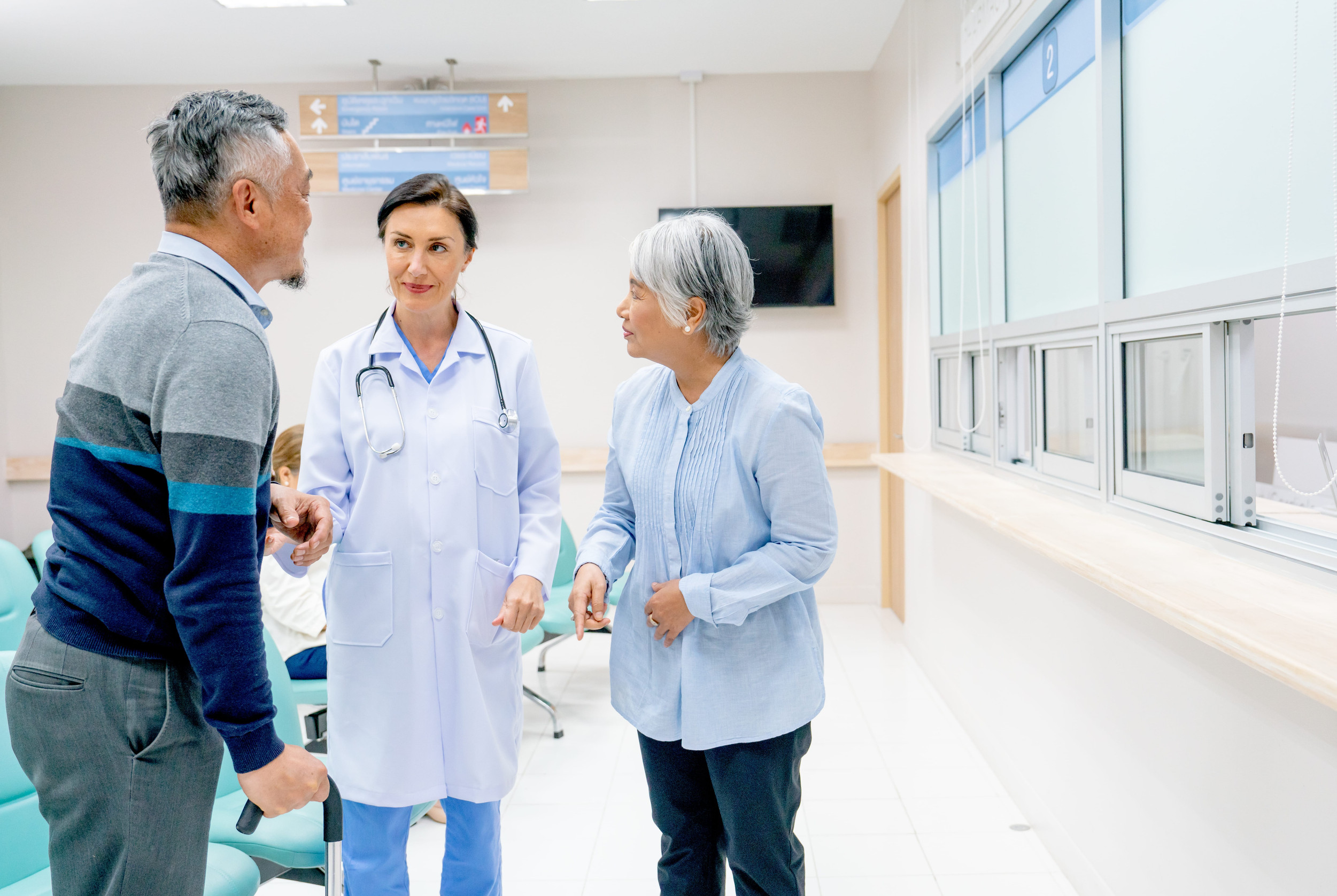 Doctor speaking with an elderly couple in a bright hospital reception area, highlighting compassionate patient care, staff communication, and a welcoming healthcare environment.